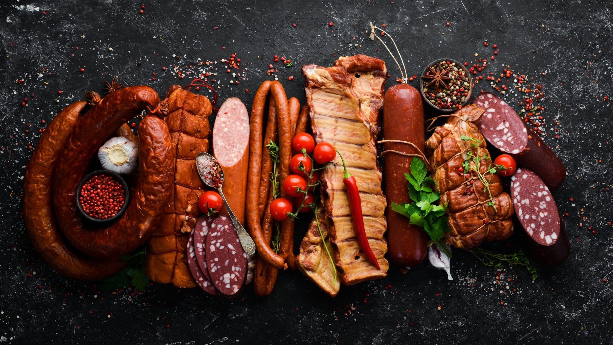 Set of sausage, salami and smoked meat with rosemary and spices on a black stone background. Top view. Free space for text.